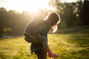 Girl giving another kid a piggy back ride in a field