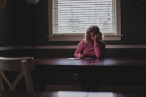 Woman writing at a table, looking tired and sad