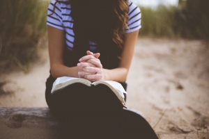 Woman praying outdoors with a bible in her lap, hands folded