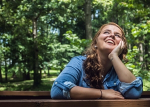 Woman sitting on a bench in the woods smiling and looking up